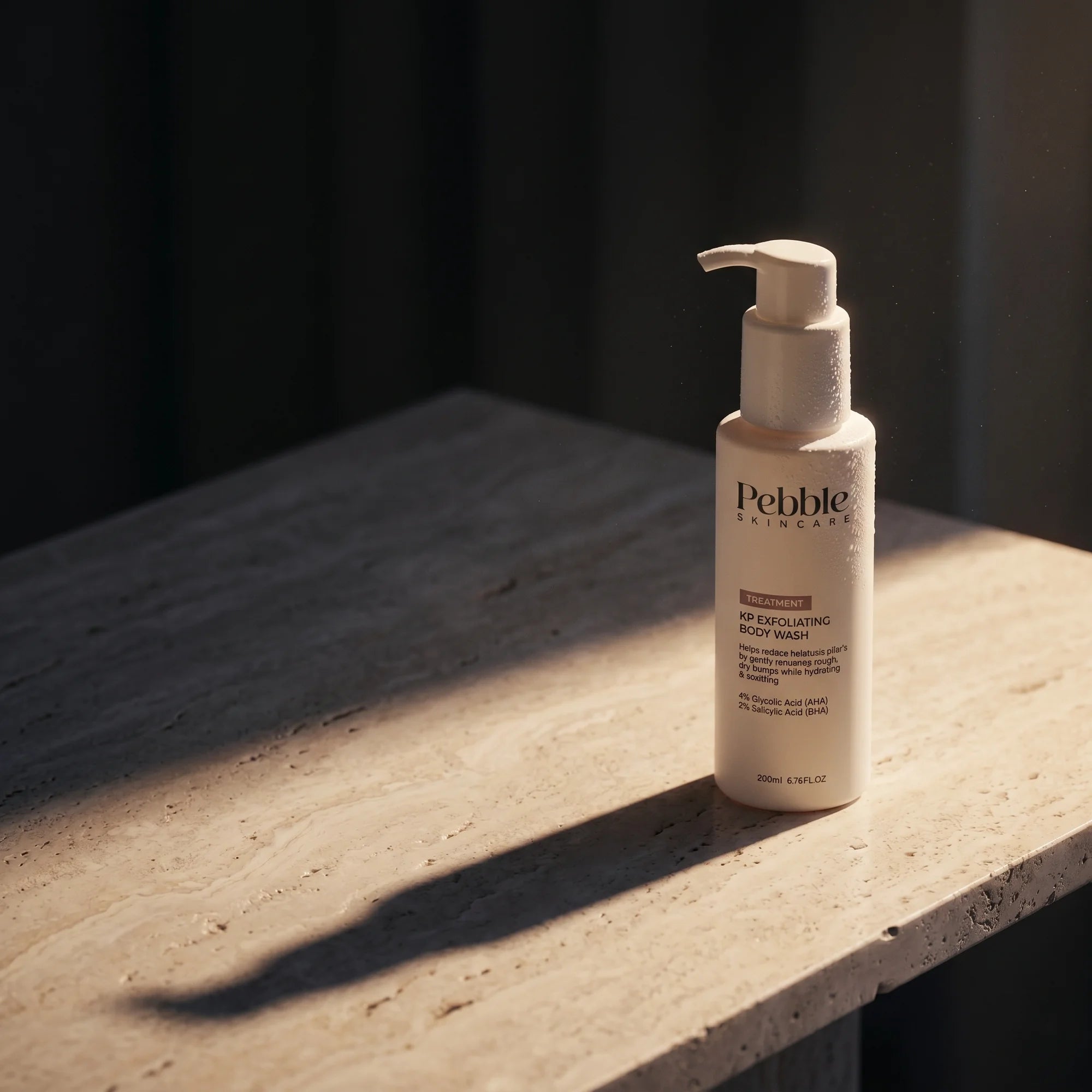 Pebble KP exfoliating body wash on travertine slab — dark cinematic raking light
