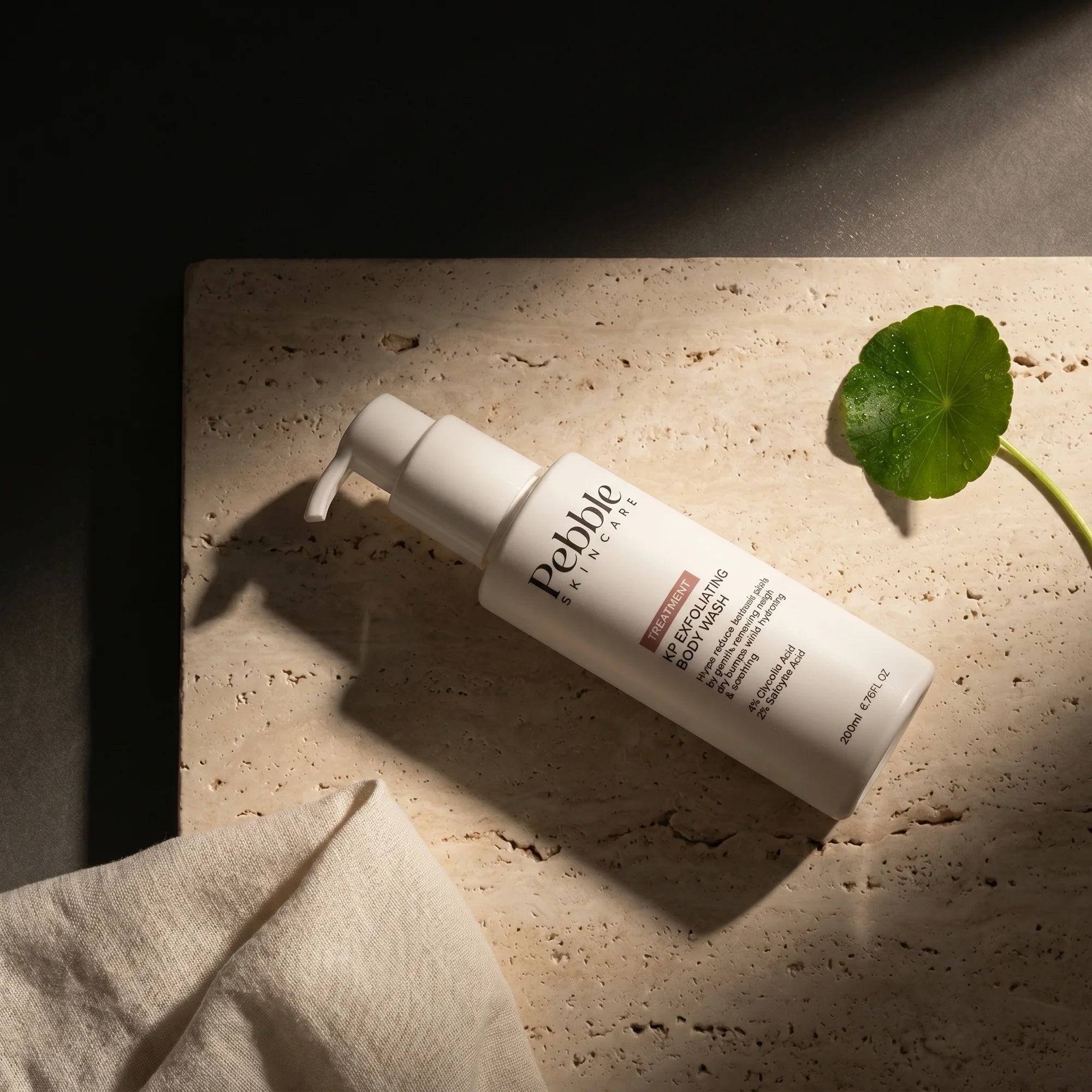 Pebble bottle flatlay on travertine with centella leaf — editorial dark hero