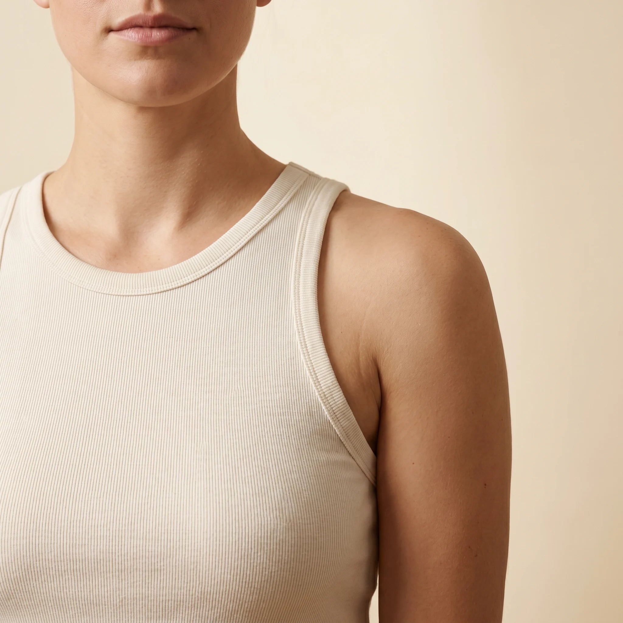 Pebble customer in cream cotton tank top — smooth shoulder and upper arm in soft window light.